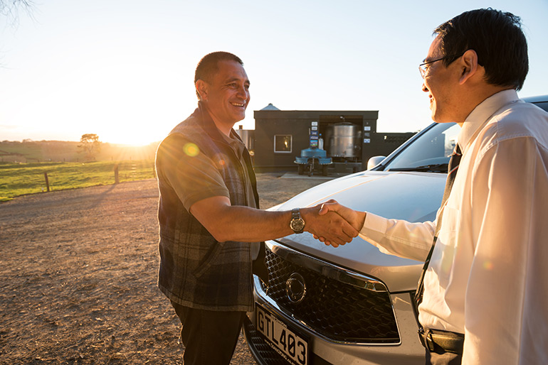 Two people shaking hands over the bonnet of a car in a rural setting