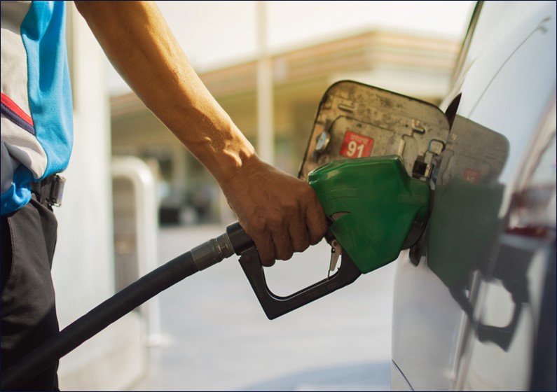 Photo of a person filling a car with petrol. The image is cropped to focus on their forearm and hand holding the handle of the nozzle against the car.