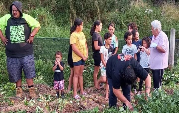 Photo: A group of children stand in a garden with their elders. There is one person bent over working in the garden, and one older woman with white hair talking to the children.   width=600 height=417 class=center ss-htmleditorfield-file image title=Photo: A group of children stand in a garden with their elders. There is one person bent over working in the garden, and one older woman with white hair talking to the children.