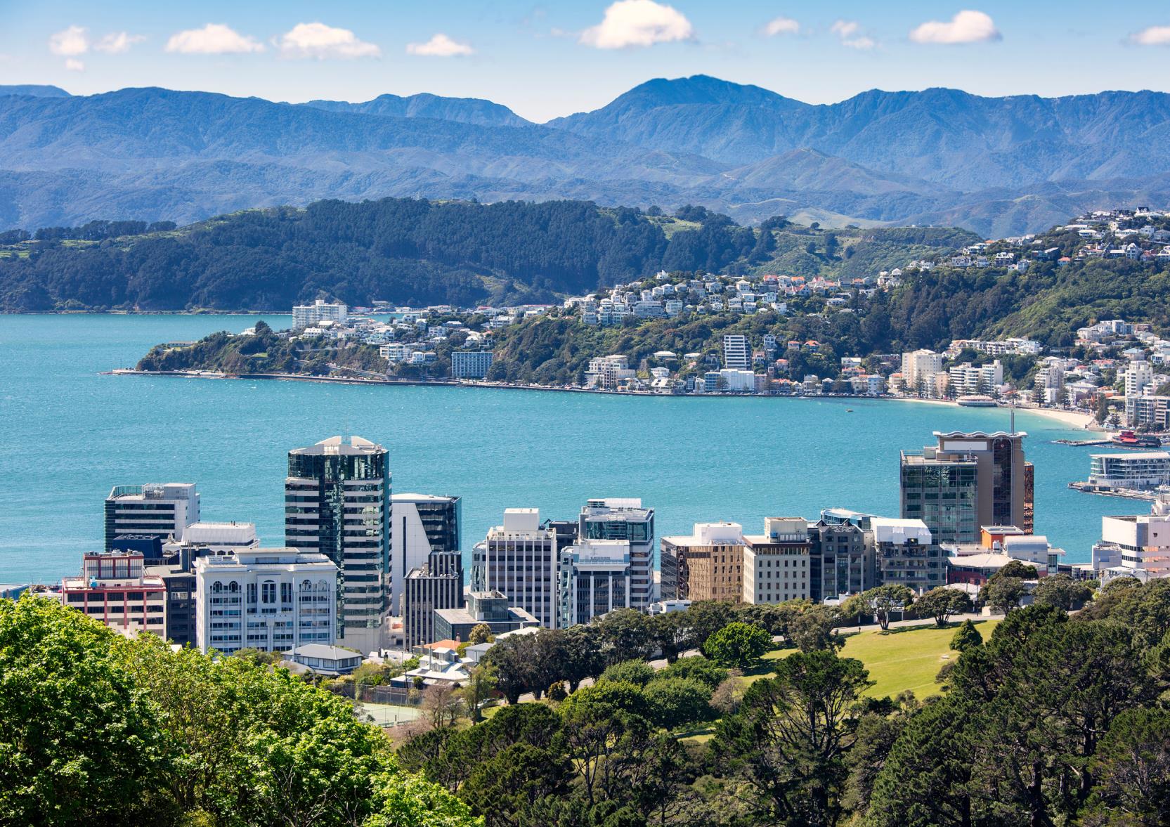 This is a decorative image. Photograph of Wellington harbour and CBD, showing lots of tall office and apartment buildings in the middle of the image, the blue water of the harbour, and the hills east of Wellington beyond.